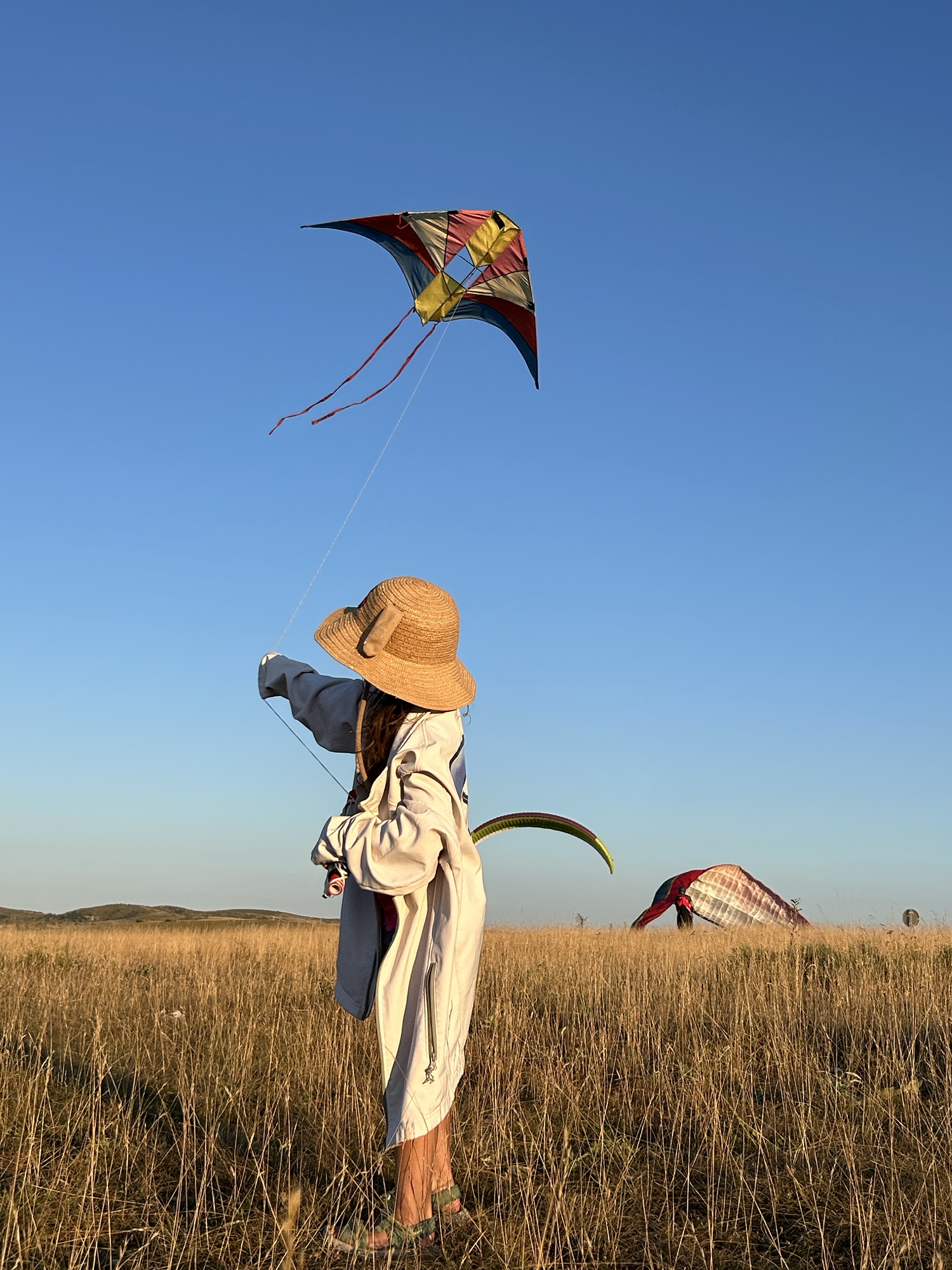 Jeune fille de dos avec une veste Volensud qui fait du cerf-volant avec parapente en fond
